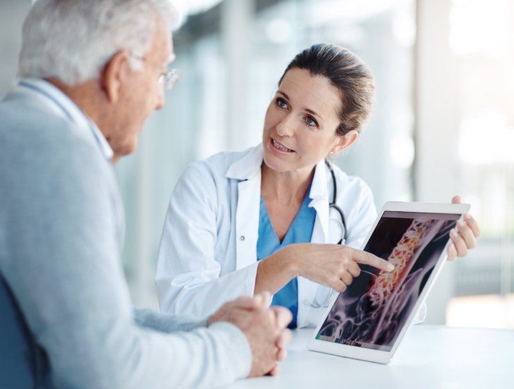 Woman Doctor talking to an older man pointing at photo of a spine on a tablet